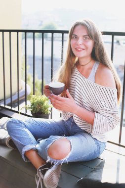 Sıcak içecek içme şehir manzaralı çatı üst terasta hipster kafede katlanmış ayaklı güzel genç kadın oturuyordu. Casual kadın içme kapuçino. Arka plan, yakın çekim, alanı Kopyala.