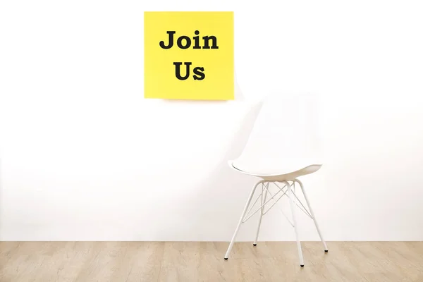 Job recruitment advertisement, JOIN US text written on yellow wall poster, one single empty loft style chair. Human resources campaign to find workers for vacant job. Close up, copy space, background.