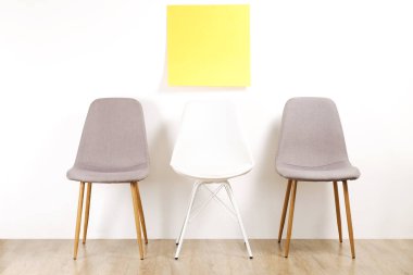 Üç kullanılabilir loft tarzı sandalye koltuk boş reklam afişi, beyaz duvar arka plan, sarı kopya alanı etiket için metin ile ahşap zemin üzerinde boş. Davet için boş pozisyon konsepti röportaj. Yakın çekim