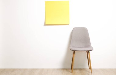 Tek boş loft tarzı gri sandalye ahşap zemin, boş reklam afiş ve beyaz duvar arka plan, metniniz için kopya alanı ile sarı etiket üzerinde. Davet için boş pozisyon konsepti röportaj. Yakın çekim.