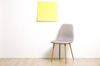 Tek boş loft tarzı gri sandalye ahşap zemin, boş reklam afiş ve beyaz duvar arka plan, metniniz için kopya alanı ile sarı etiket üzerinde. Davet için boş pozisyon konsepti röportaj. Yakın çekim.