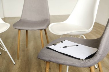 Birden çok loft tarzı boş sandalye ahşap zemin, danışmanının koltuk Pano ve notlar için kalem satırındaki ayakta. Grup terapisi için bağımlıları ve alkolikler konsept danışmanlık. Alan arka plan kopya, yakın çekim