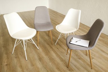 Birden çok loft tarzı boş sandalye ahşap zemin, danışmanının koltuk Pano ve notlar için kalem satırındaki ayakta. Grup terapisi için bağımlıları ve alkolikler konsept danışmanlık. Alan arka plan kopya, yakın çekim