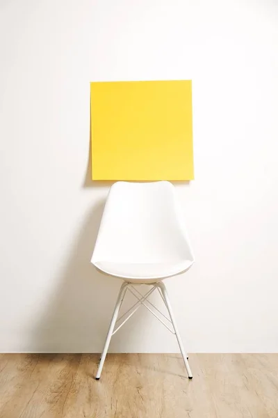 Single empty loft style chair on wooden floor with blank ad poster and white wall background, yellow sticker with copy space for your text. Interview invitation for vacant position concept. Close up.