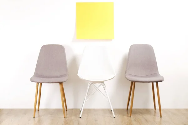 stock image Three empty available loft style chair seats on wooden floor with blank ad poster, white wall background, yellow copy space sticker for text. Interview invitation for vacant position concept. Close up