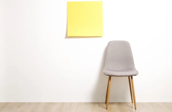 Single empty loft style gray chair on wooden floor, blank ad poster and white wall background, yellow sticker with copy space for your text. Interview invitation for vacant position concept. Close up.