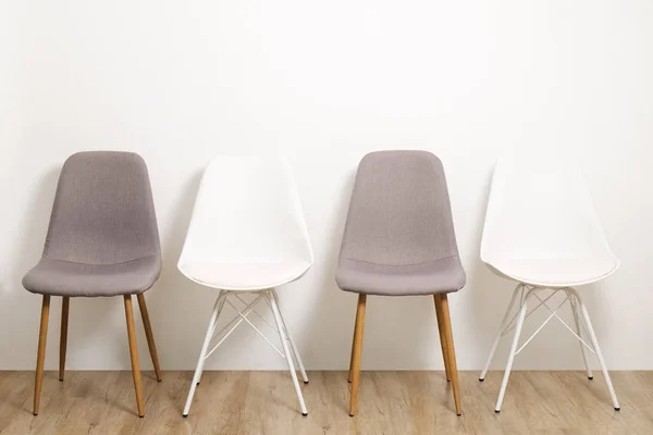 Multiple white gray elegant loft style empty chairs standing in room, wooden floor & big blank wall background with a lot of copy space for text. Vacant seats. Human resources hiring campaign concept