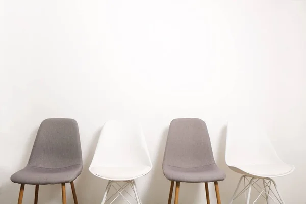 Multiple white gray elegant loft style empty chairs standing in room, wooden floor & big blank wall background with a lot of copy space for text. Vacant seats. Human resources hiring campaign concept