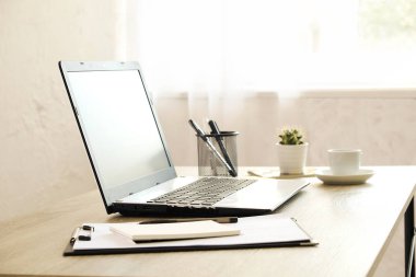 Boş ekran dizüstü bilgisayar, fincan cappuccino kahve, kaktüs, sarf malzemeleri ve katlanmış gözüne gözlük güneş ışığı tam geniş ofiste ahşap masa üzerinde. Yaratıcı çalışma alanı. Yakın çekim, uzay, arka plan kopya