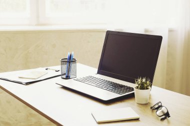 Dizüstü bilgisayar, pano, kaktüs ev bitki, sarf malzemeleri ve geniş Office güneş ışığı tam ahşap masa üzerinde katlanmış gözlük. Tasarımcının yaratıcı çalışma alanı kavramı. Yakın çekim, uzay, arka plan kopya.