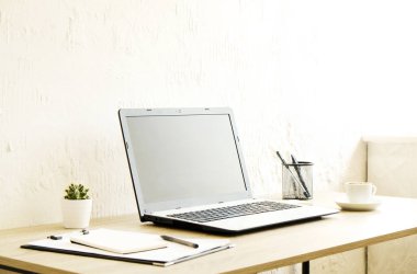Boş ekran dizüstü bilgisayar, fincan cappuccino kahve, kaktüs, sarf malzemeleri ve katlanmış gözüne gözlük güneş ışığı tam geniş ofiste ahşap masa üzerinde. Yaratıcı çalışma alanı. Yakın çekim, uzay, arka plan kopya