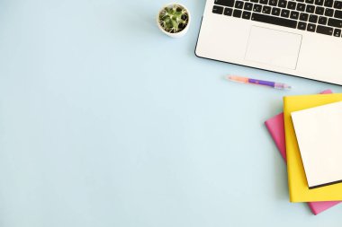 Ofis İşyeri dizüstü bilgisayar, birden çok renkli Notebook, yeşil kaktüs bitki, kahve, sarf malzemeleri ve kırtasiye mavi zemin üzerine beyaz fincan ile. Yakın çekim, kopya alanı, üstten görünüm, düz lay.