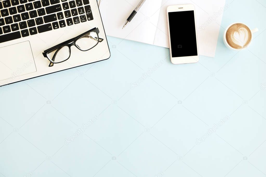 Minimalistic flat lay composition of black & white laptop computer keyboard, cell phone gadget, cup of coffee & folded glasses on blue surface desk table background. Workspace top view, copy space