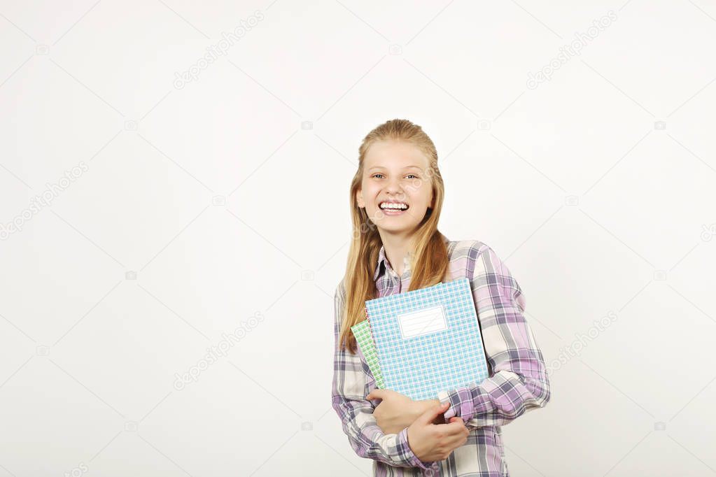 Beautiful blonde teenage girl with charming smile in schoolgirl uniform wearing pleated skirt, white shirt, holding notebooks. Back to school sale concept. Background, copy space, close up, isolated.