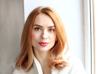 Kış sonbahar sezonu beyaz örgü kazak ve büyük gevşek eşarp omuzlarında giyen güzel kızıl saçlı Genç kadın kahve dükkanı, pencerenin yanında oturan dudaklarında kırmızı ruj. Arka plan, yakın çekim.