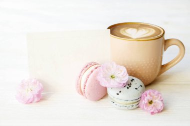 Yaban mersini ve Fransız macaron çöl kek, kahverengi kalp şeklinde kapuçino içecek ve latte sanat ile kahve fincanı, bahar çiçekli çilek aromalı. İzole beyaz arka plan, yakın çekim, kopya alanı