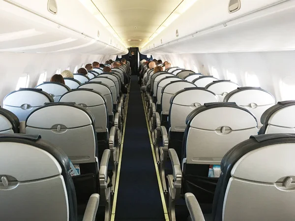 Rows of black leather seats and illuminator windows down the aisle in commercial aircraft cabin. Economy class chairs of airplane. Background, copy space, close up.
