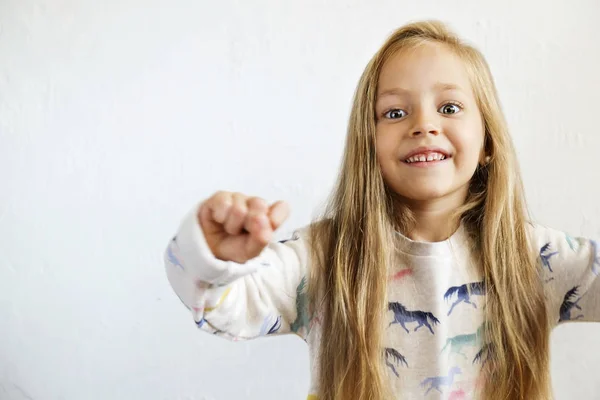 Little blonde girl with long golden hair dancing, smling and having fun over white textured plaster wall background. Five years old blonde female child posing. Copy space for text.