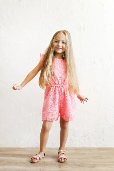 Little blonde girl with long golden hair dancing, smling and having fun over white textured plaster wall background. Five years old blonde female child posing. Copy space for text.