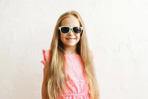 小女孩长着金色的长发 穿着时髦的休闲服装 戴着墨镜 微笑着 做着滑稽的面孔 五岁的女儿穿着粉红色的衣服摆姿势 复制空间 — 图库照片