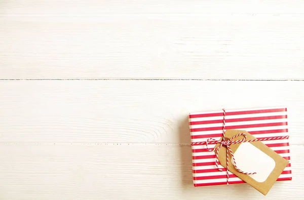 Christmas and new year present wrapped in festive colorful red and white stripes paper. Single holiday gift box with blank name tag on wooden texture table. Close up, background, copy space, top view.