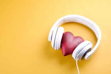 Senin kalp kavramı dinle. Parlak sarı zemin üzerinde beyaz kulaklık ile büyük kırmızı kalp. Sevgililer günü kompozisyon kulaklık ve kalp. Yakın çekim, kopya alanı, üstten görünüm, düz lay,