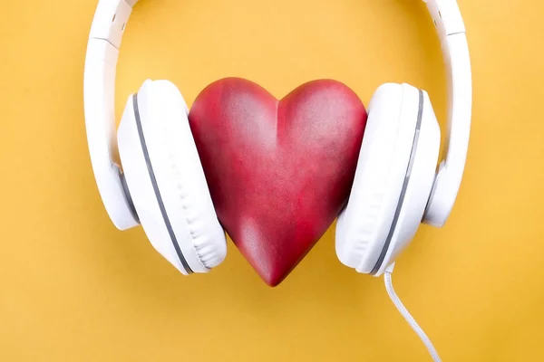 あなたの心の概念に耳を傾けます 明るい黄色の背景に白いヘッドフォンで大きな赤いハート 聖バレンタインの日組成ヘッドセットと心 クローズ アップ コピー スペース 平面図 フラット レイアウト — ストック写真