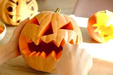 Genç kadının Jack O Lattern onun ahşap mutfak masasında bıçakla olgun Turuncu kabak oyma kapatın. Tüm hazırlama kadın Havva Halloween parti süslemeleri toplantı salonu. Arka plan, kopya alanı.