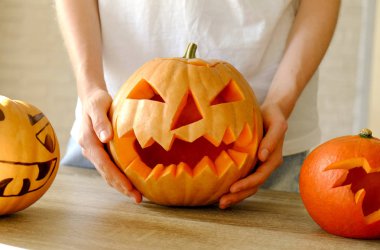 Genç kadının Jack O Lattern onun ahşap mutfak masasında bıçakla olgun Turuncu kabak oyma kapatın. Tüm hazırlama kadın Havva Halloween parti süslemeleri toplantı salonu. Arka plan, kopya alanı.