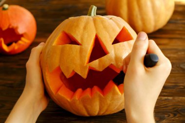 Genç kadının Jack O Lattern onun ahşap mutfak masasında bıçakla olgun Turuncu kabak oyma kapatın. Tüm hazırlama kadın Havva Halloween parti süslemeleri toplantı salonu. Arka plan, kopya alanı.
