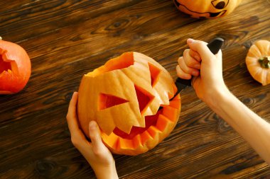 Genç kadının Jack O Lattern onun ahşap mutfak masasında bıçakla olgun Turuncu kabak oyma kapatın. Tüm hazırlama kadın Havva Halloween parti süslemeleri toplantı salonu. Arka plan, kopya alanı.