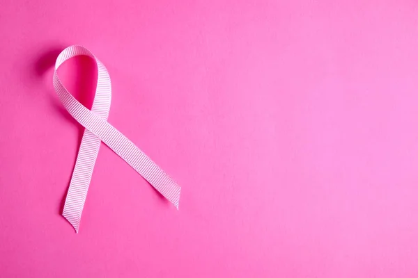 The pink colored ribbon - international symbol of breast cancer awareness and moral support for women. Isolated background, copy space, close up, top view fat lay.