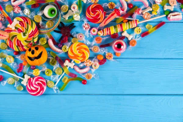 Assorted teeth and eyeball shaped candy spread on wooden table, jelly spider, gummy worms, round lollipop and other mixed candy on blue wood background. Top view, copy space, close up, flat lay.