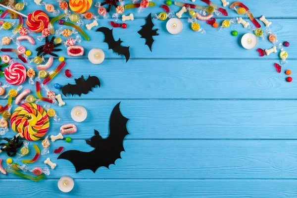 Assorted teeth and eyeball shaped candy spread on wooden table, jelly spider, gummy worms, round lollipop and other mixed candy on blue wood background. Top view, copy space, close up, flat lay.