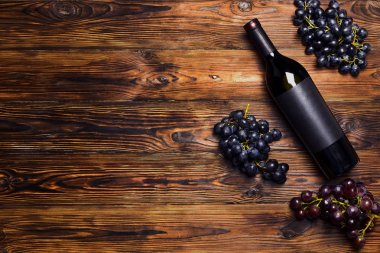 Kırmızı vintage açılmamış şişe boş mat siyah etiket ile şarap ve ahşap masa arka plan üzerinde Olgun üzüm demet. Pahalı bir şişe cabernet sauvignon kavramı. Alan, en iyi görünüm düz lay kopyalama