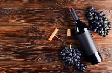 Vintage boş mat siyah etiketli, kırmızı şarap şişe düşünüp ve ahşap masa arka plan üzerinde üzüm demet. Pahalı bir şişe cabernet sauvignon kavramı. Kopyalama alanı, üstten görünüm, düz lay.