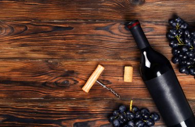 Vintage boş mat siyah etiketli, kırmızı şarap şişe düşünüp ve ahşap masa arka plan üzerinde üzüm demet. Pahalı bir şişe cabernet sauvignon kavramı. Kopyalama alanı, üstten görünüm, düz lay.