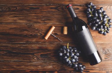 Vintage boş mat siyah etiketli, kırmızı şarap şişe düşünüp ve ahşap masa arka plan üzerinde üzüm demet. Pahalı bir şişe cabernet sauvignon kavramı. Kopyalama alanı, üstten görünüm, düz lay.