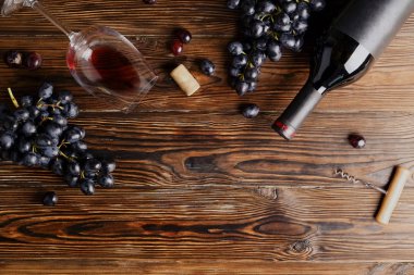 Vintage boş mat siyah etiketli, kırmızı şarap şişe düşünüp ve ahşap masa arka plan üzerinde üzüm demet. Pahalı bir şişe cabernet sauvignon kavramı. Kopyalama alanı, üstten görünüm, düz lay.