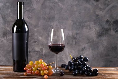 Vintage şişe boş mat siyah etiketli, ahşap masa, beton duvar arka plan üzerinde üzüm demet kırmızı şarap. Pahalı bir şişe cabernet sauvignon kavramı. Kopyalama alanı, üstten görünüm, düz lay.