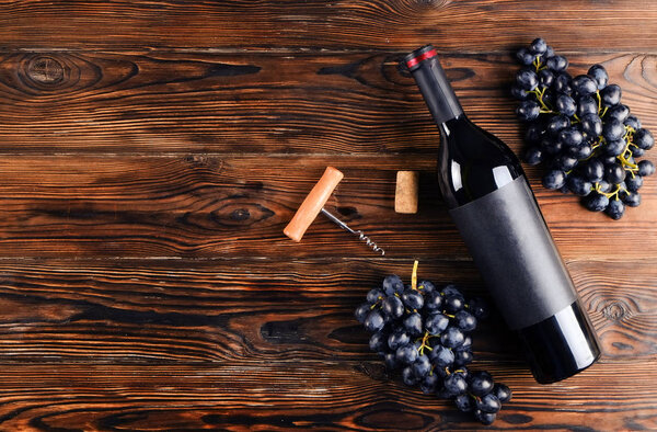 Винтажная бутылка красного вина с чистой матовой черной этикеткой, штопор & гроздья винограда на деревянном фоне стола. Дорогую бутылку каберне совиньон концепции. Копировальное пространство, вид сверху, плоская кладка
.