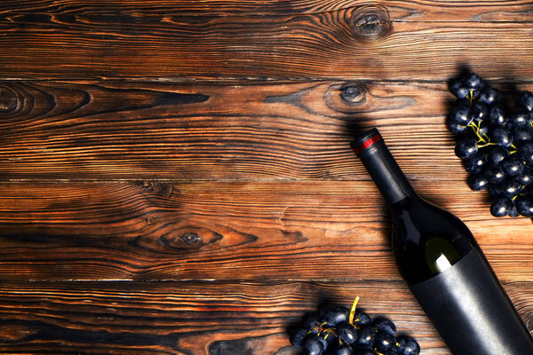 Нераспечатанная винтажная бутылка красного вина с чистой матовой черной этикеткой и гроздьями спелого винограда на деревянном столе. Дорогую бутылку каберне совиньон концепции. Пространство для копирования, плоский вид сверху
