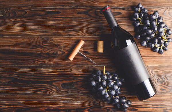 Винтажная бутылка красного вина с чистой матовой черной этикеткой, штопор & гроздья винограда на деревянном фоне стола. Дорогую бутылку каберне совиньон концепции. Копировальное пространство, вид сверху, плоская кладка
.