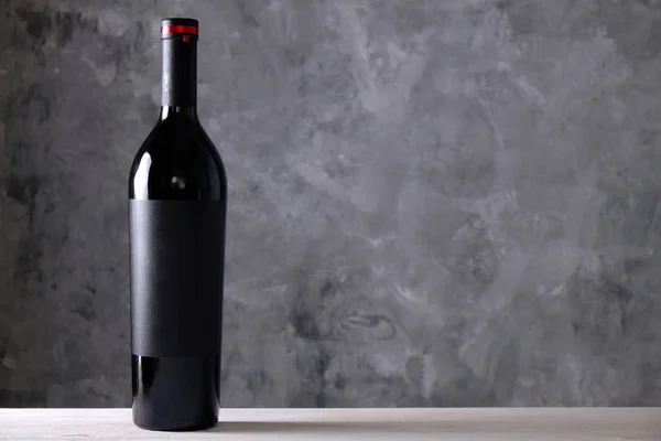 Vintage bottle of red wine with blank matte black labe on wooden table, concrete wall background. Expensive bottle of cabernet sauvignon concept. Copy space, top view, close up.