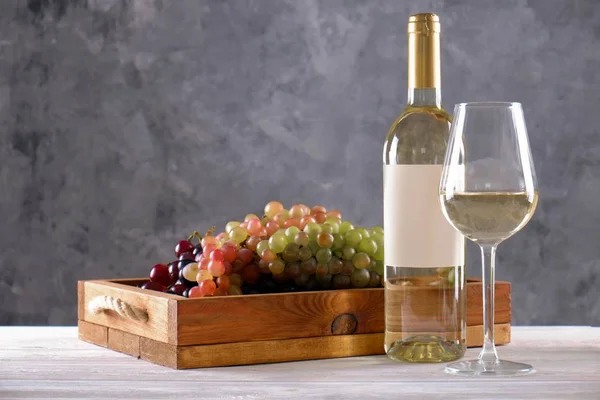 Vintage bottle of white wine with blank matte label, bunch of different grapes on wooden table, concrete background. Expensive bottle of shardonnay concept. Copy space, top view, flat lay, close up.