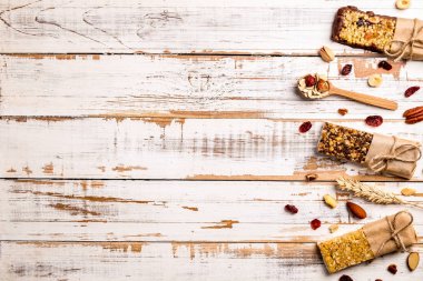 Çeşitli granola çikolata enerji barlar satırda dağınık karışık Kuruyemiş, tahıllar ve kuru meyve, grunged Beyaz ahşap masa arka plan ile. Sağlıklı vegan fitness gıda aperatif. Üstten Görünüm, kopya alanı, kapat.
