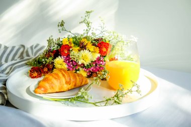 Yatak konsepti Odaya Servis Kahvaltı. Beyaz tepsi ile bardağı taze portakal suyu ve Fransız kruvasan simit, soyulmuş battaniye, renkli widflowers dolu. Üstten görünüm, arka plan, kapatmak, alanı Kopyala.