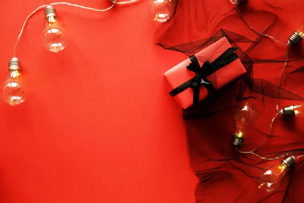 Beautiful festive composition in shades of red. Beautiful present wrapped in crimson wrapping paper, tied with black silk ribbon with loft lights. Background, copy space, top view, flat lay, close up.