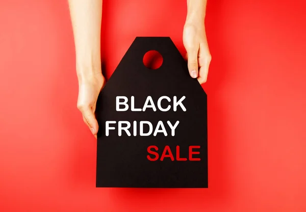 Black friday sale concept. Fourth Friday of November, beginning of Christmas shopping season since 1952. Black tag with white text on bright red background. Copy space, close up, top view, flat lay.