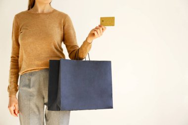Klasik şık kıyafet, kahverengi süveter ve gevşek gri pantolon alışverişe gitti genç ince kadın, holding kağıt torba ve VIP altın kredi / bankamatik kartı. Beyaz arka plan, kopya alanı, yakın çekim.